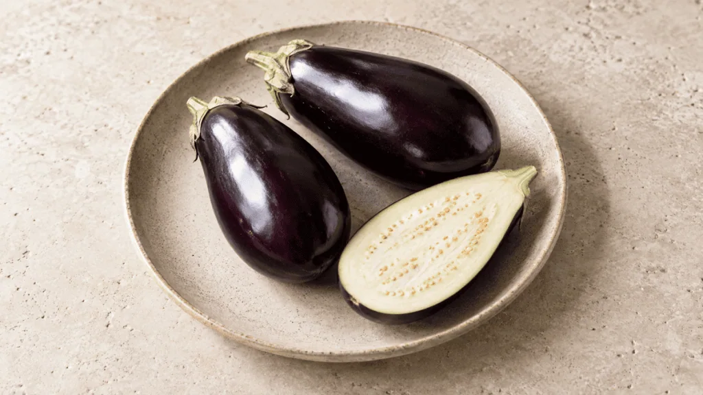 Aubergines fraîches entières et coupées sur une assiette en grès