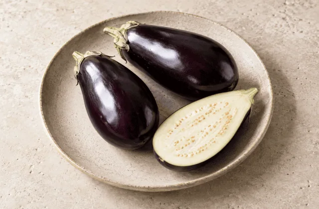 Aubergines fraîches entières et coupées sur une assiette en grès
