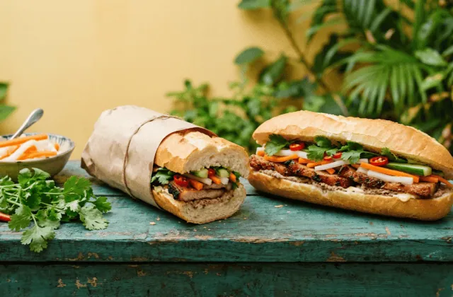 Deux bánh mì garnis de porc caramélisé, pickles de carotte et daïkon, concombre, coriandre et piment, l’un emballé dans du papier kraft