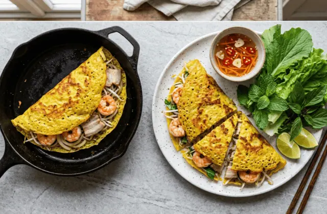 Bánh xèo aux crevettes et au porc maison, dans la poêle et coupé en parts, avec nước chấm et herbes fraîches