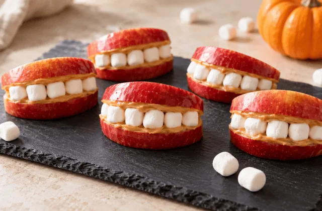 Dentiers croquants en pomme rouge, beurre de cacahuète et dents de mini-guimauves sur une ardoise