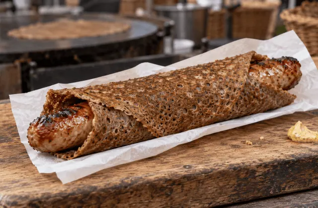 Galette-saucisse bretonne servie dans un papier sur un marché