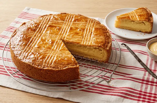 Gâteau basque à la crème pâtissière sur une grille, dessus doré quadrillé, part coupée montrant la crème vanillée