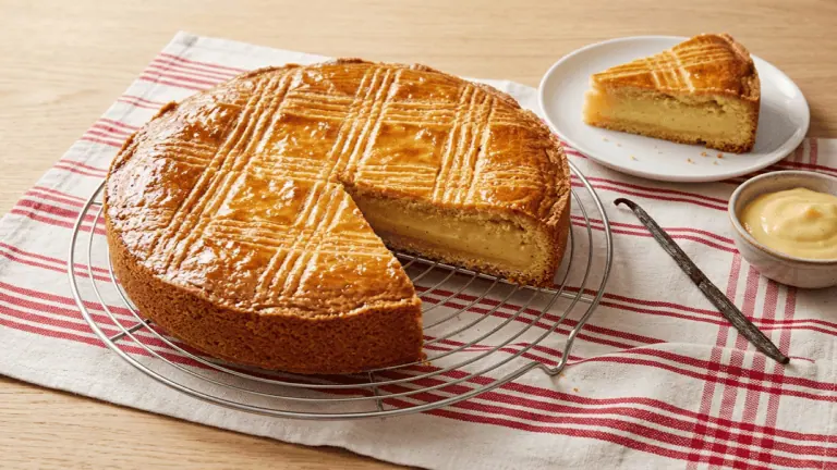 Gâteau basque à la crème pâtissière sur une grille, dessus doré quadrillé, part coupée montrant la crème vanillée