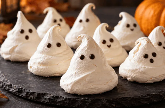 Meringues fantômes blanches aux yeux en chocolat présentées sur une ardoise sombre