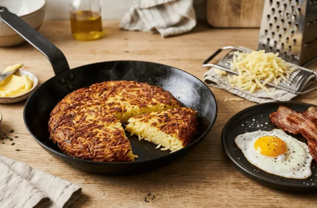 Rösti de pommes de terre doré et croustillant dans une poêle, part coupée, œuf au plat et bacon, râpe à côté