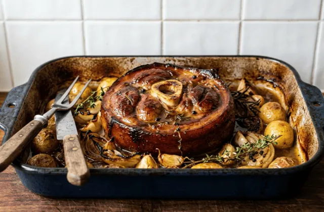 Rouelle de porc braisée au four dans un plat émaillé, oignons confits, ail, pommes de terre et thym dans le jus