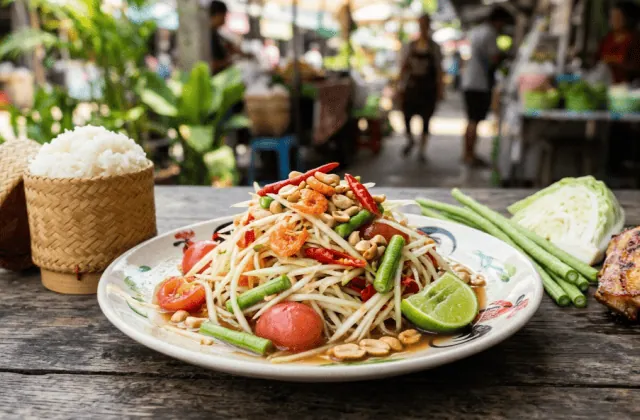 Assiette de som tam : papaye verte râpée, tomates cerises, haricots kilomètre, cacahuètes, crevettes séchées et piment, avec riz gluant et poulet grillé